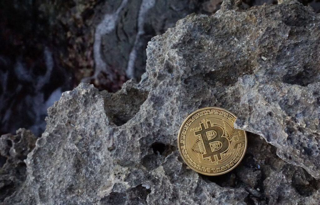 Bitcoin sitting on rocks above crashing ocean wave Ⓒ 2023 – Crypto Coin Opps