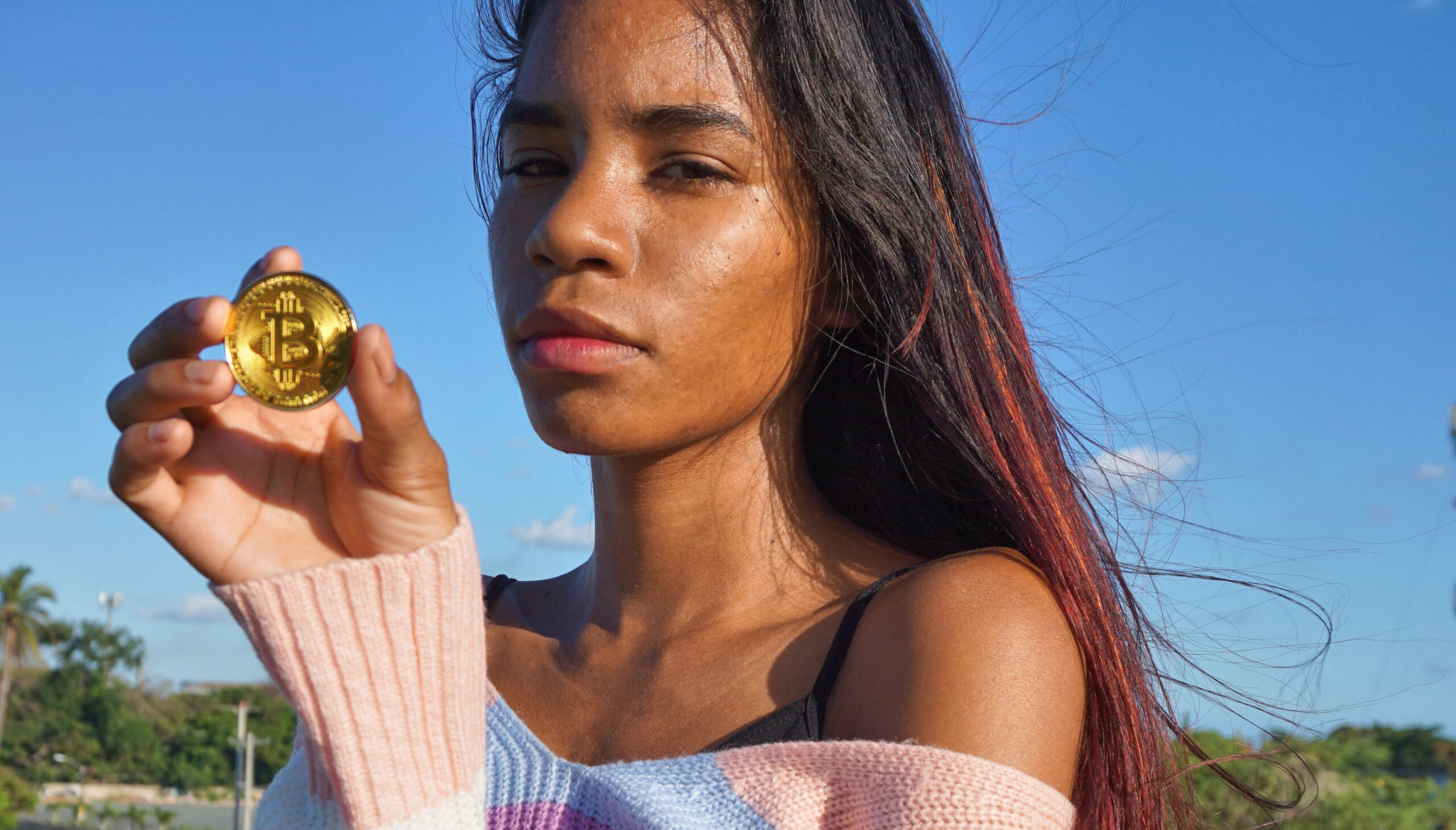 Dominican Girl Holds a Bitcoin ($BTC) Token Ⓒ 2023 – Crypto Coin Opps
