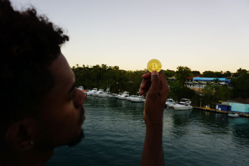 Young Man Looks At Bitcoin Token On Emilio-Prud'Homme Bridge in La Romana, Dominican Republic